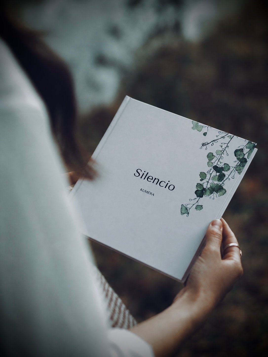 Una mujer sostiene el libro Silencio de KUMERA entre las manos, al aire libre.