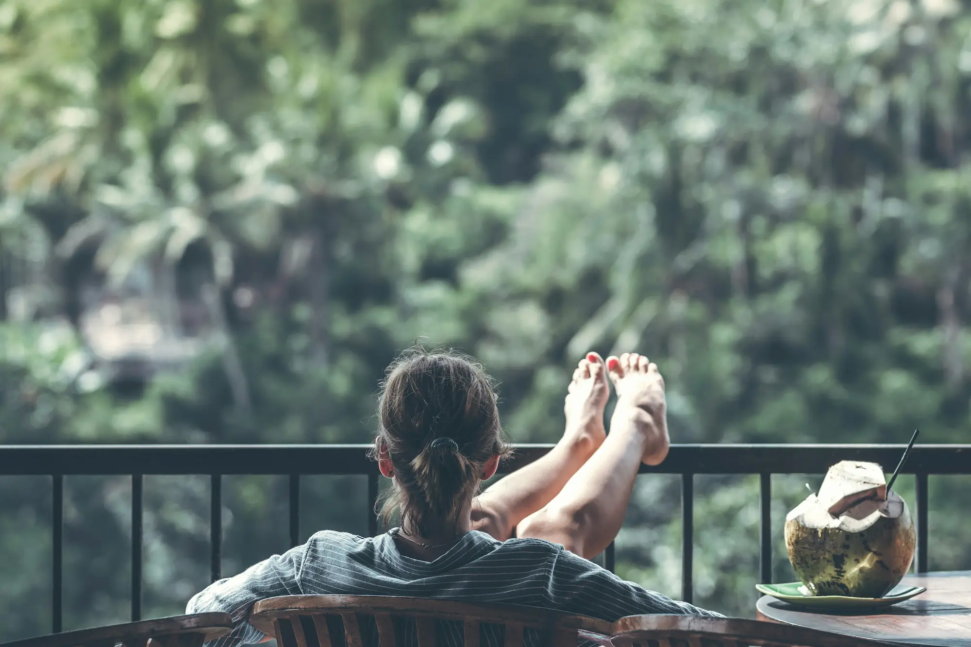 Une personne se repose sur un balcon, les pieds sur la rambarde, face à la végétation