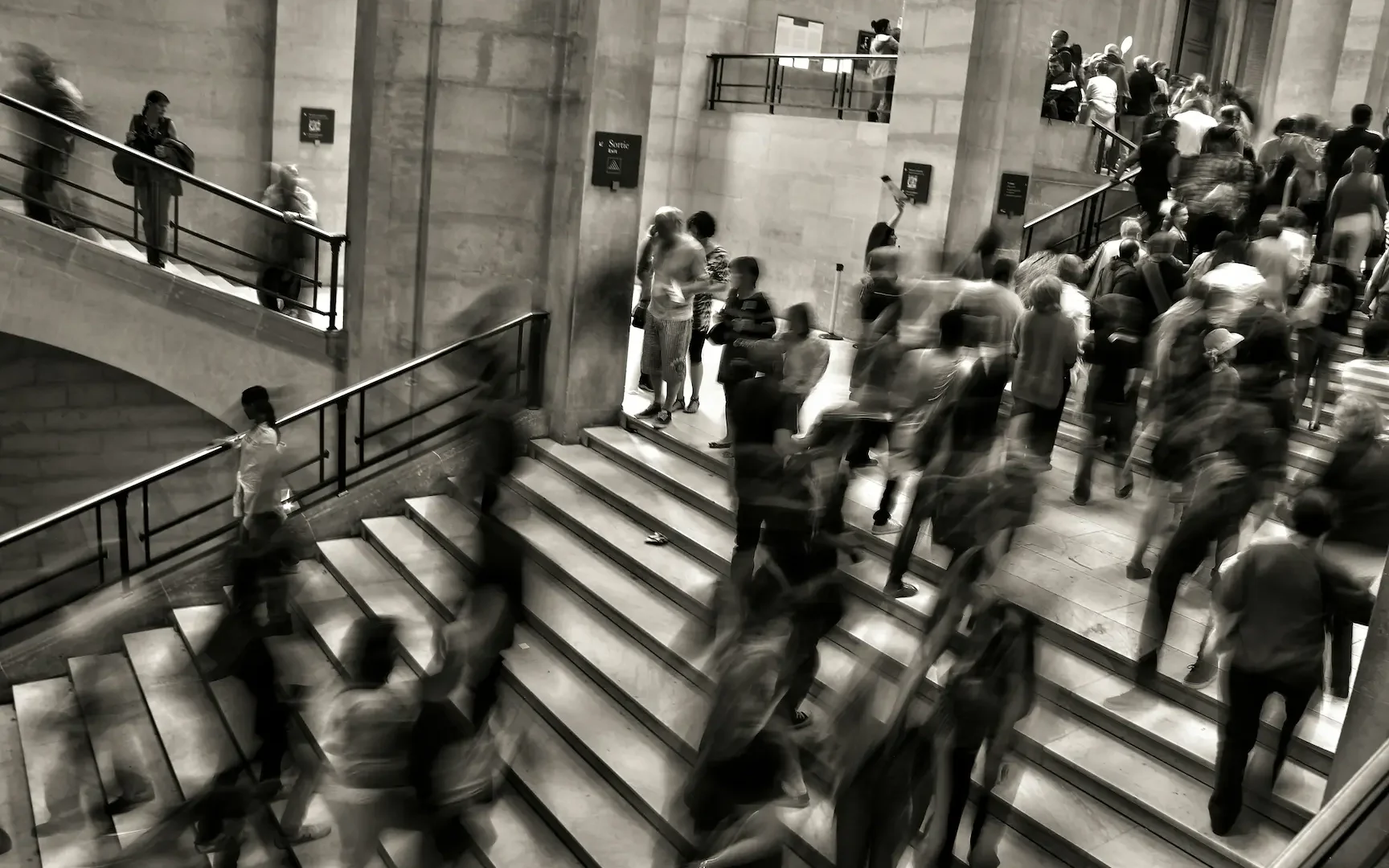 Multitud borrosa subiendo y bajando unas escaleras de piedra, en blanco y negro