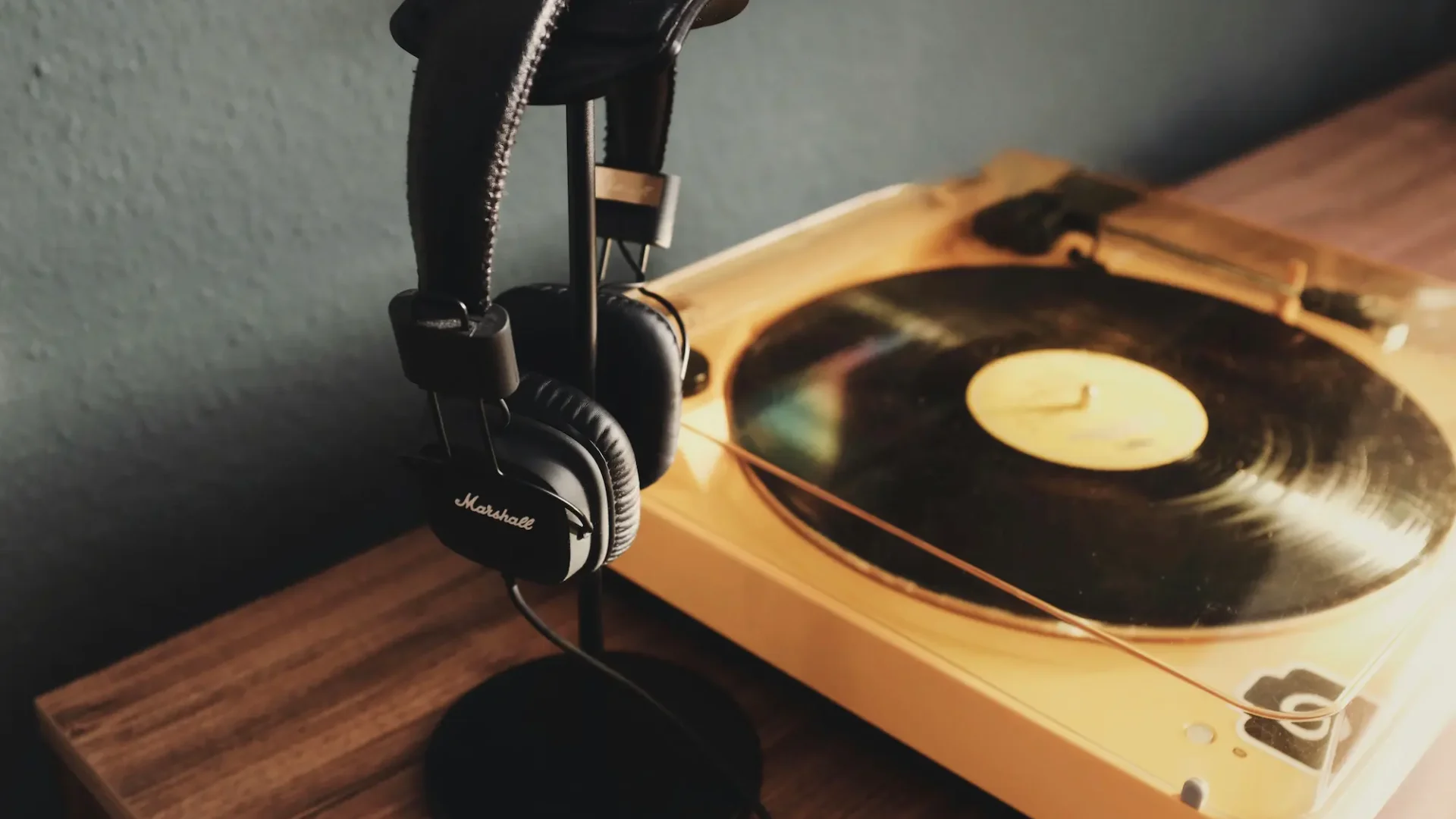 Unos auriculares colgados de un soporte junto a un tocadiscos con un vinilo